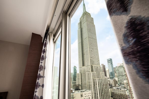 Une vue sur l’Empire State Building, prise depuis une fenêtre avec un rideau.