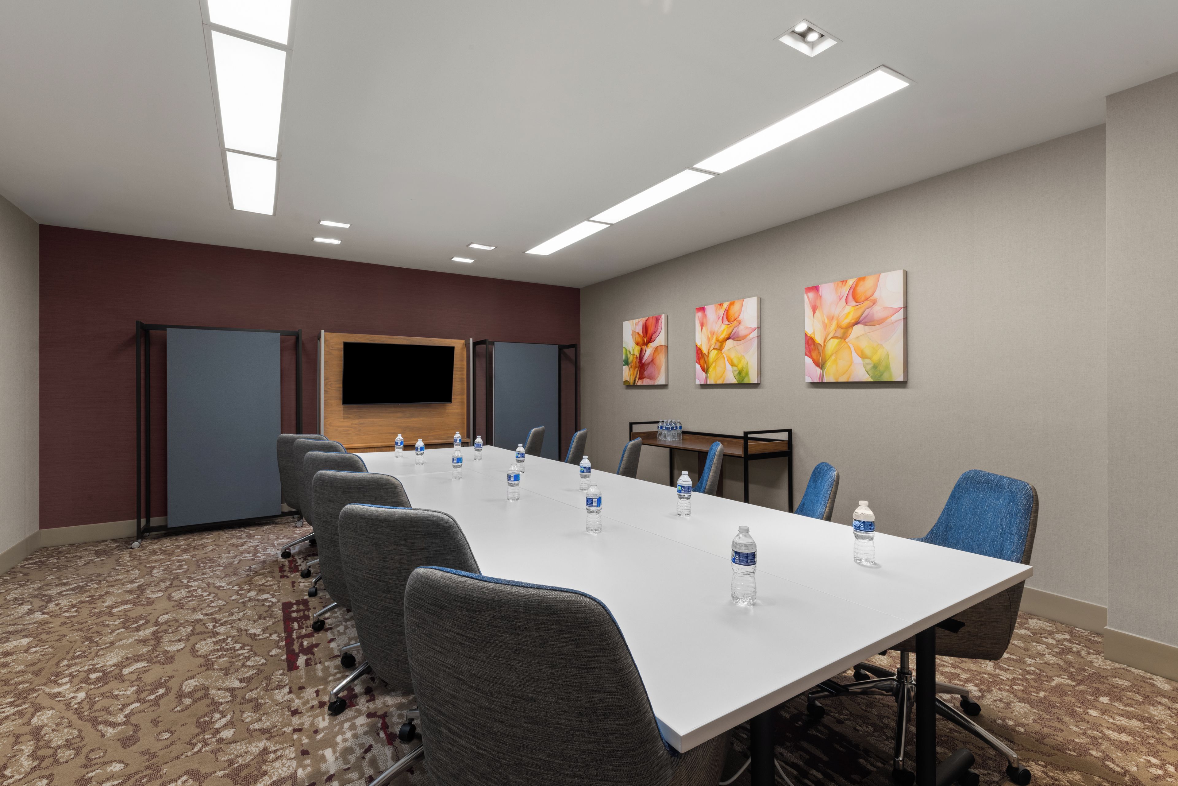 A conference room with a long table, chairs, water bottles, a flat-screen TV, and abstract art on the wall.