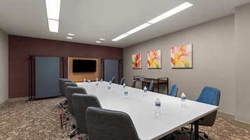 A conference room with a long table, chairs, water bottles, a flat-screen TV, and abstract art on the wall.
