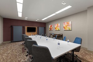 Een vergaderruimte met een lange tafel, stoelen, waterflesjes, een flatscreen-tv en abstracte kunst aan de muur.