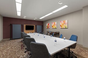 A conference room with a long table, chairs, water bottles, a flat-screen TV, and abstract art on the wall.