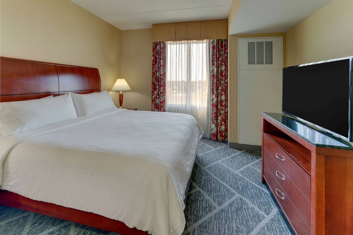 Une chambre d’hôtel avec un grand lit, une télévision, une commode et une fenêtre avec des rideaux.