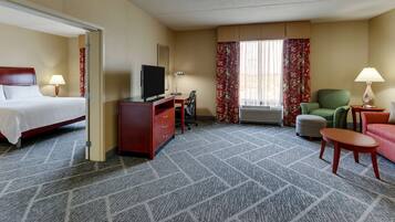 A hotel room with a bed, desk, chair, TV, and a small table.