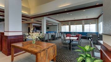 A spacious hotel lobby with a wooden reception desk, seating areas, and large windows providing natural light.