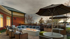 An outdoor patio with a fire pit, seating area, and umbrellas. - Hilton Garden Inn Indianapolis Airport (Indianapolis)