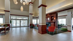 A spacious lobby with high ceilings, large windows, and a seating area with red and green chairs. - Hilton Garden Inn Indianapolis Airport (Indianapolis)
