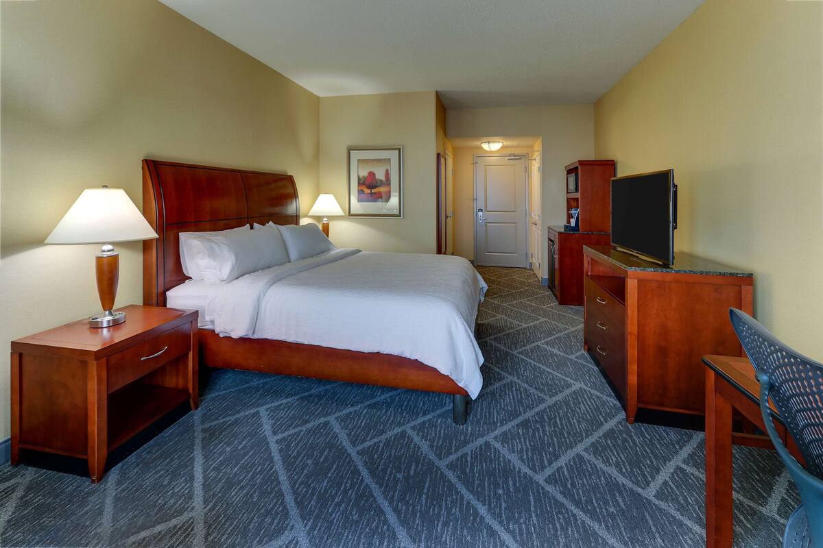 Une chambre d’hôtel équipée d’un lit, d’un bureau, d’une chaise, d’une télévision et d’une porte donnant accès à une salle de bain.