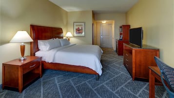 A hotel room with a bed, a desk, a chair, a TV, and a door leading to a bathroom.