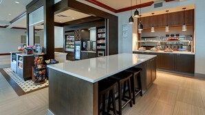 A modern kitchen with a central island, bar stools, and a refrigerator. - Hilton Garden Inn Indianapolis Airport (Indianapolis)