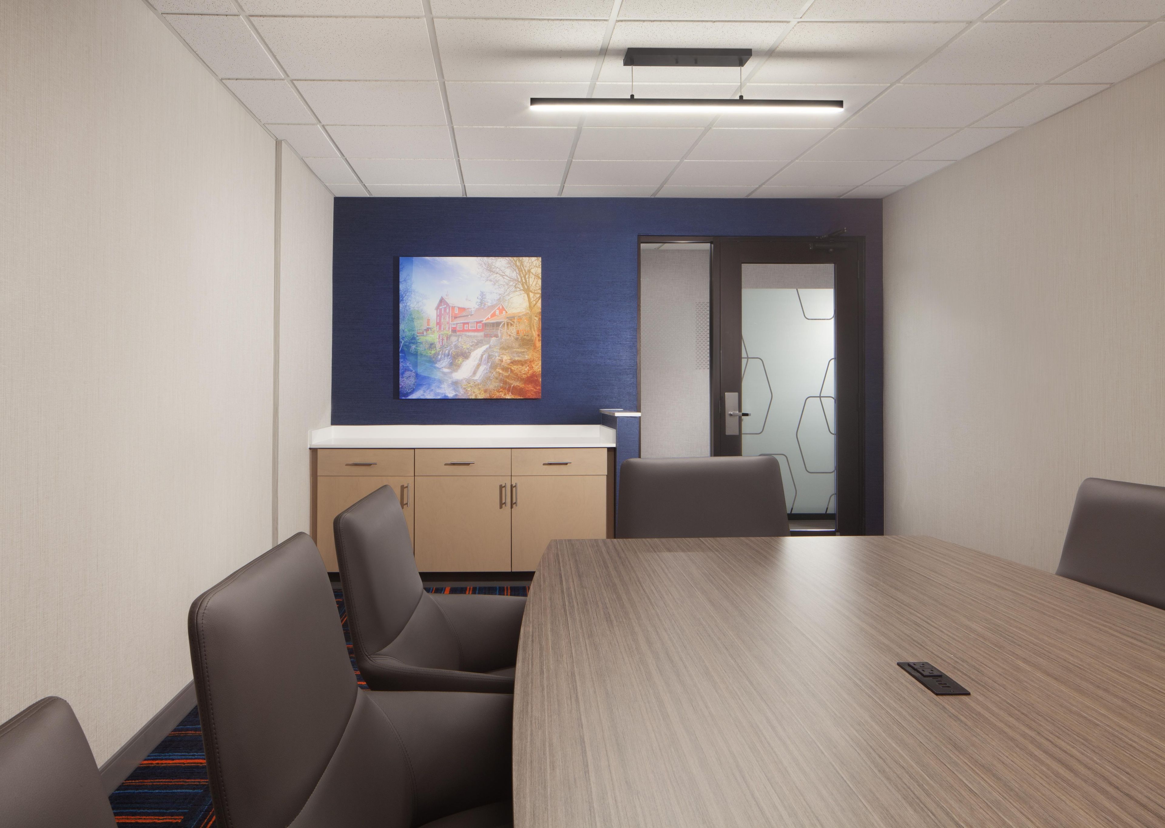 Een vergaderruimte met een grote tafel, stoelen, een schilderij aan de muur en een deur naar een andere ruimte.