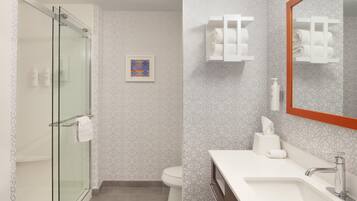 Un baño moderno con cabina de ducha de vidrio, inodoro y lavamanos con espejo.