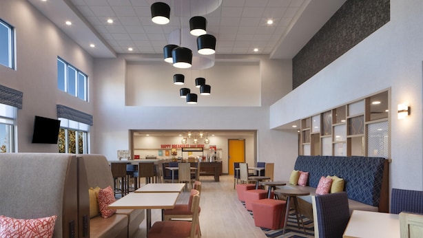 A modern hotel lobby with seating areas, a central dining space, and a TV mounted on the wall. - Hampton Inn & Suites Cleveland Mentor (Mentor)