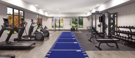 Un gimnasio con cintas de correr, máquinas elípticas, una pista de atletismo azul, equipo de levantamiento de pesas y ventanas amplias.