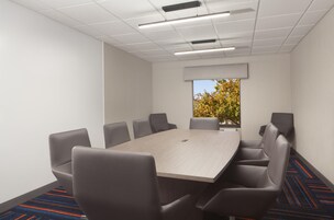 A conference room with a rectangular table, six chairs, and a large window with a view of trees.