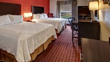A hotel room with two beds, a desk, a chair, a TV, and a window with a view.