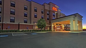 Ein Hampton Inn & Suites Hotel mit moderner Fassade, blauem Himmel und gut beleuchtetem Eingang.