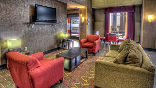 Eine Hotelhalle mit einem an der Wand befestigten Flachbildfernseher, einem roten Sessel, einem beigen Sofa und einem gemusterten Teppich.