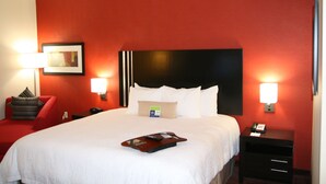 Ein Hotelzimmer mit einem großen Bett, roten Wänden, einem schwarzen Kopfteil und einem roten Sessel.