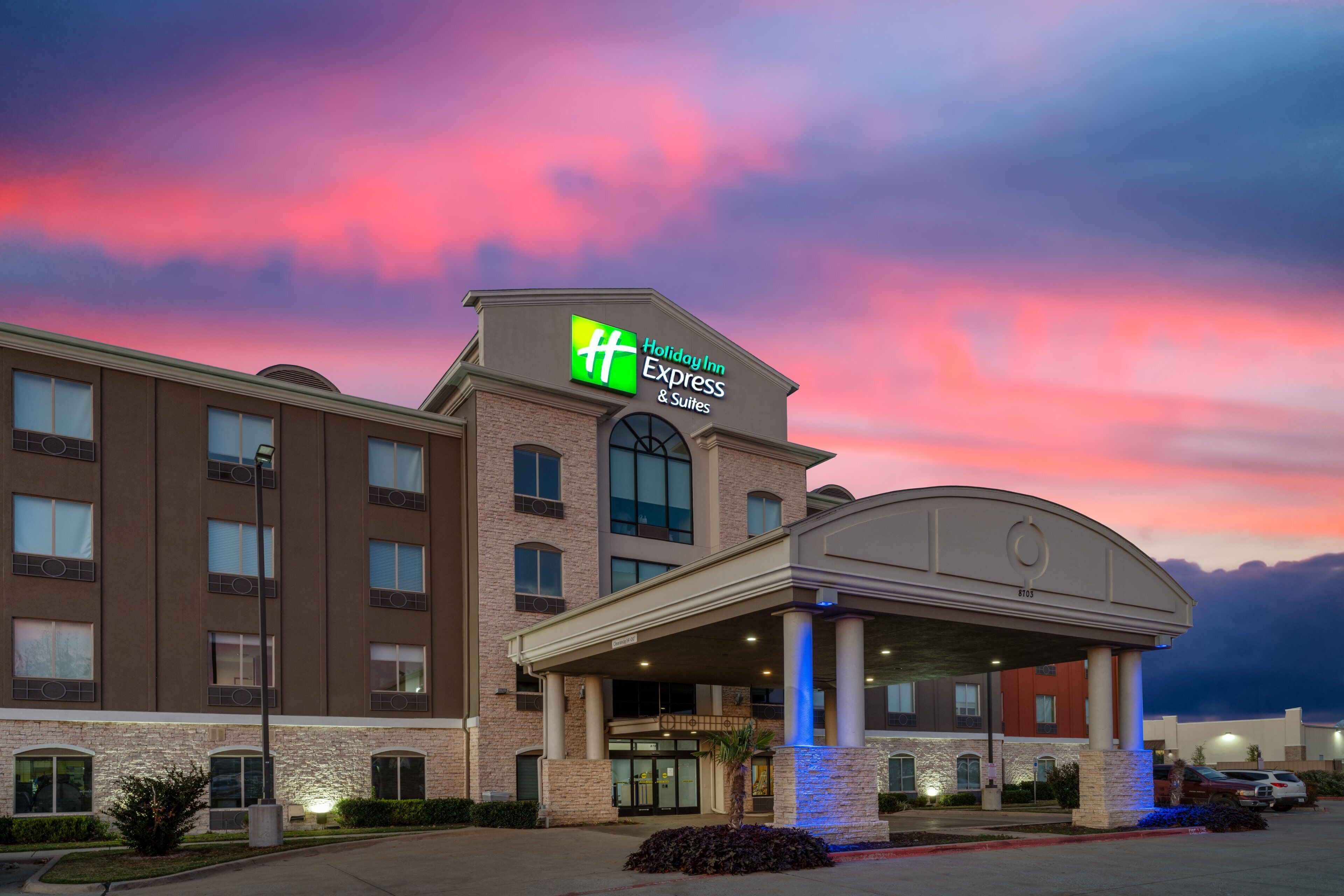A Holiday Inn Express & Suites building with a brick facade, large windows, and a covered entrance area.