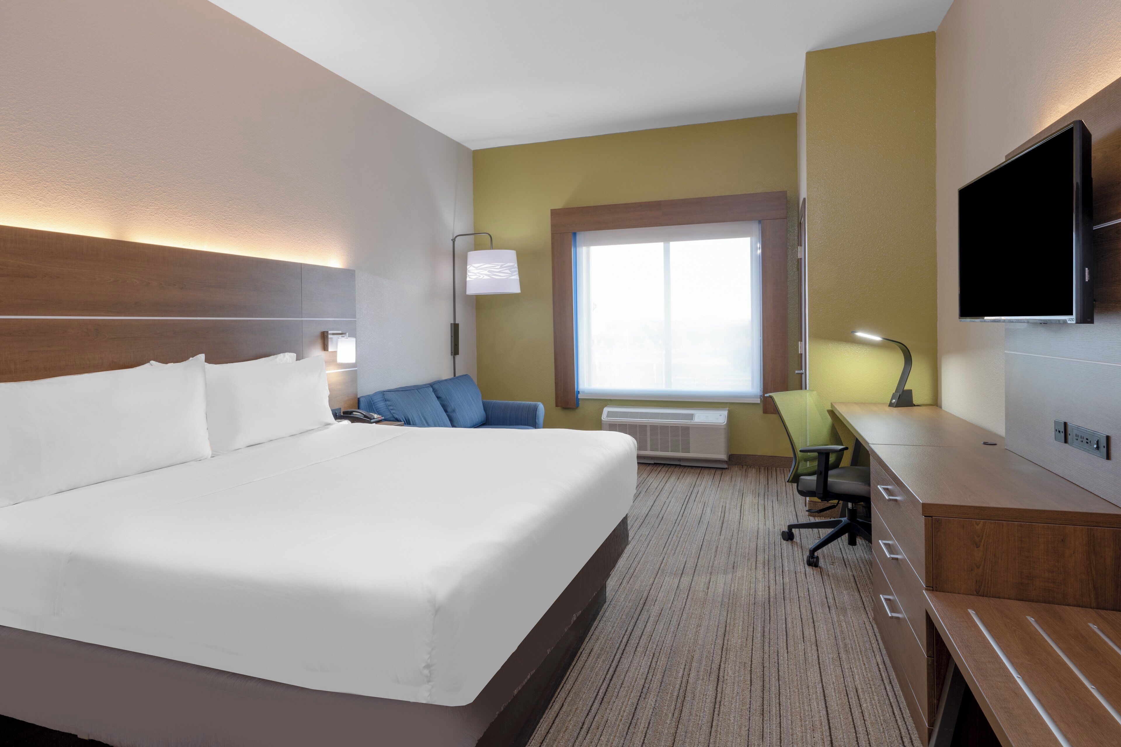 A hotel room with a large bed, a desk, a chair, a television, and a window.