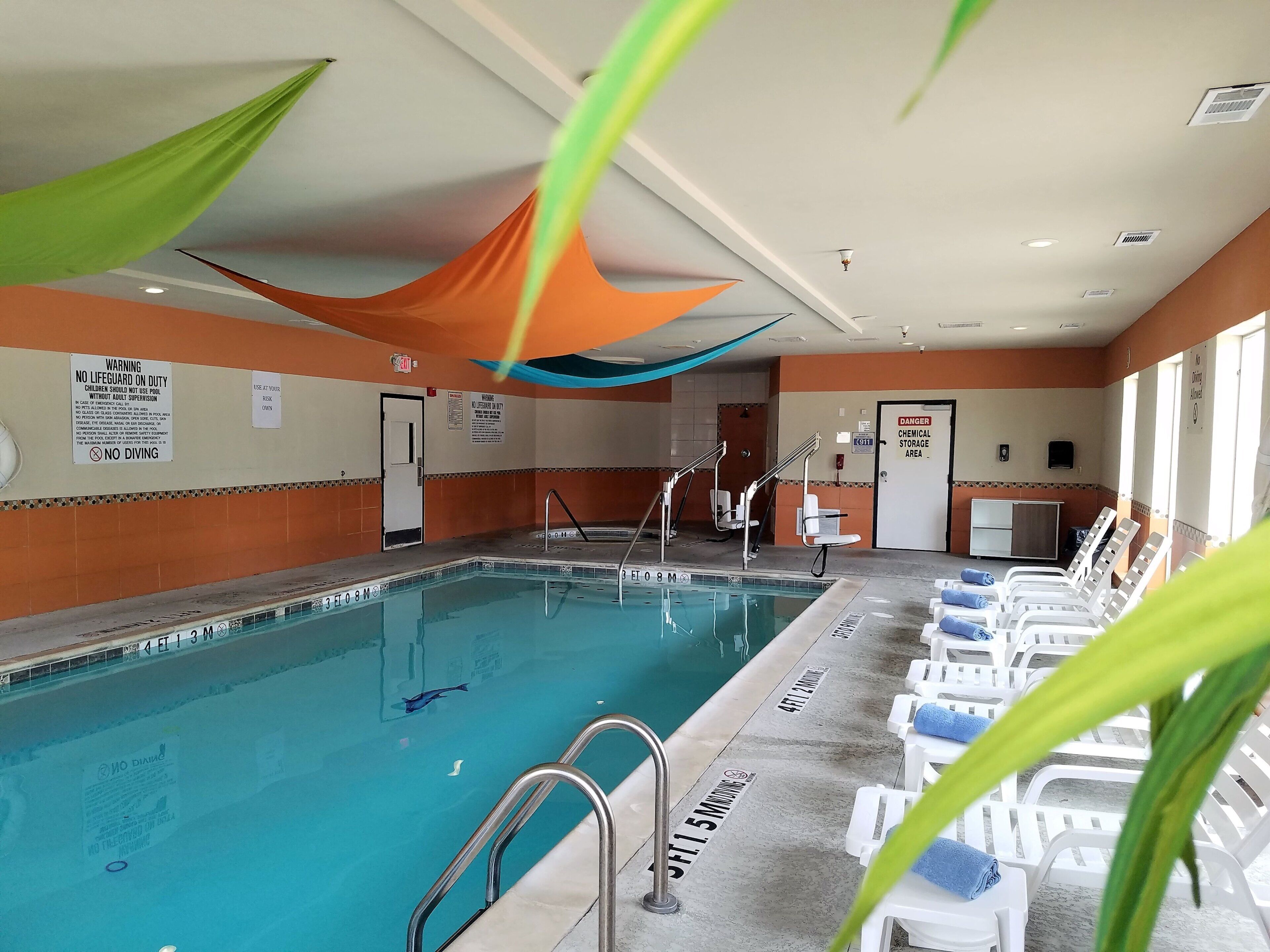 An indoor swimming pool with safety signs, a lifeguard chair, and lounge chairs.