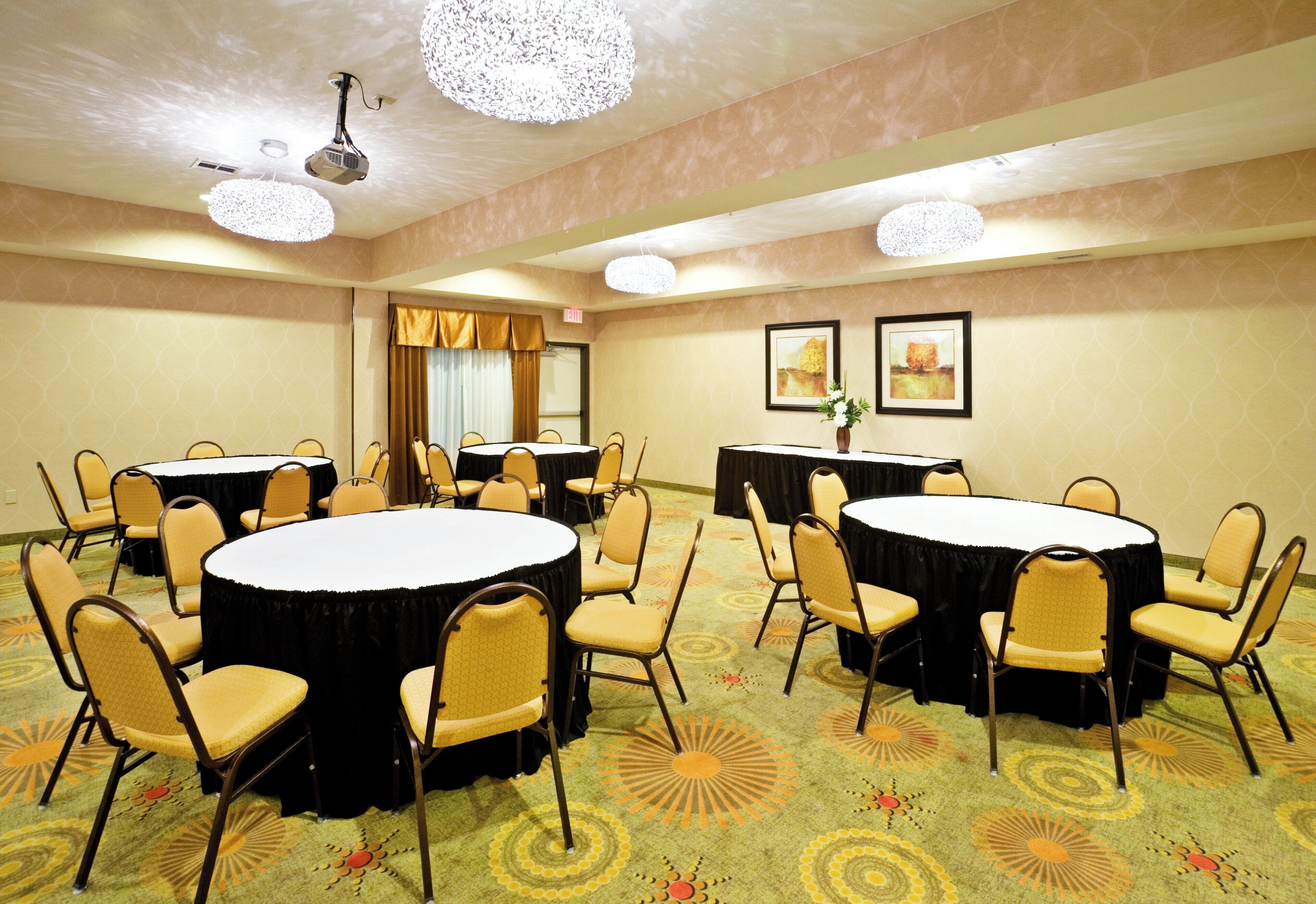 A conference room with round tables and chairs, a projector, and framed artwork on the walls.