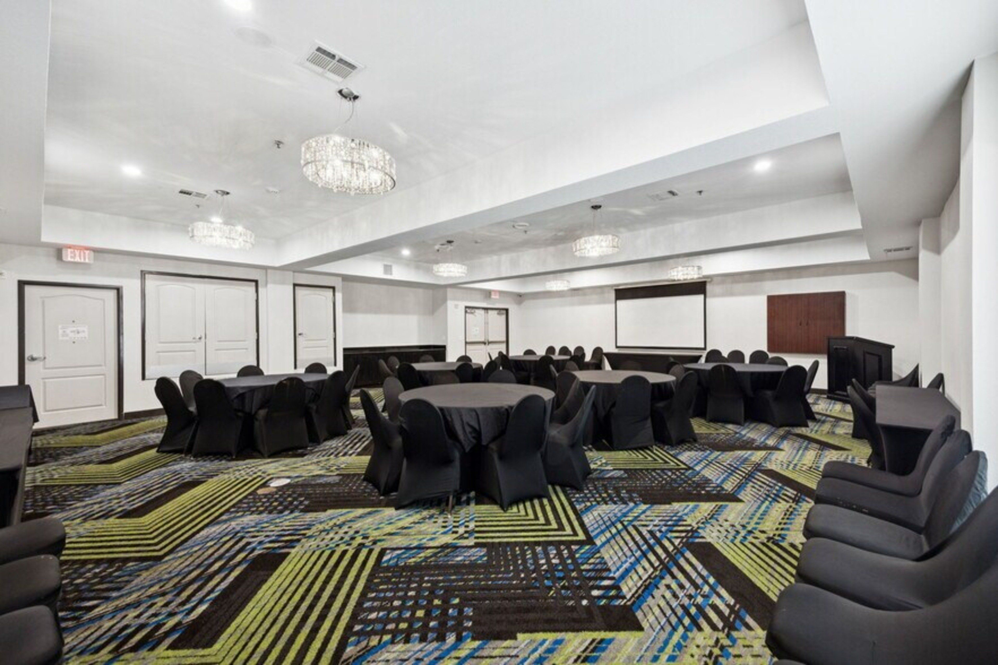 Un salón de conferencias con mesas redondas, sillas negras, alfombra estampada y un candelabro.