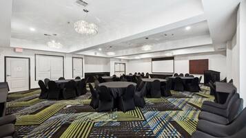 Un salón de conferencias con mesas redondas, sillas negras, alfombra estampada y un candelabro.