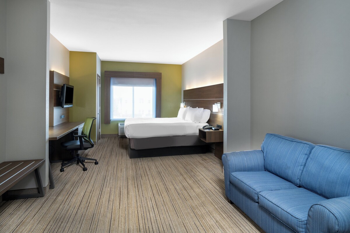 A hotel room with a bed, a desk with a chair, a blue sofa, and a television on the wall.