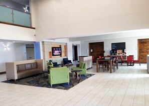 Um hall amplo com área de estar, um bar de café e uma televisão fixada na parede.