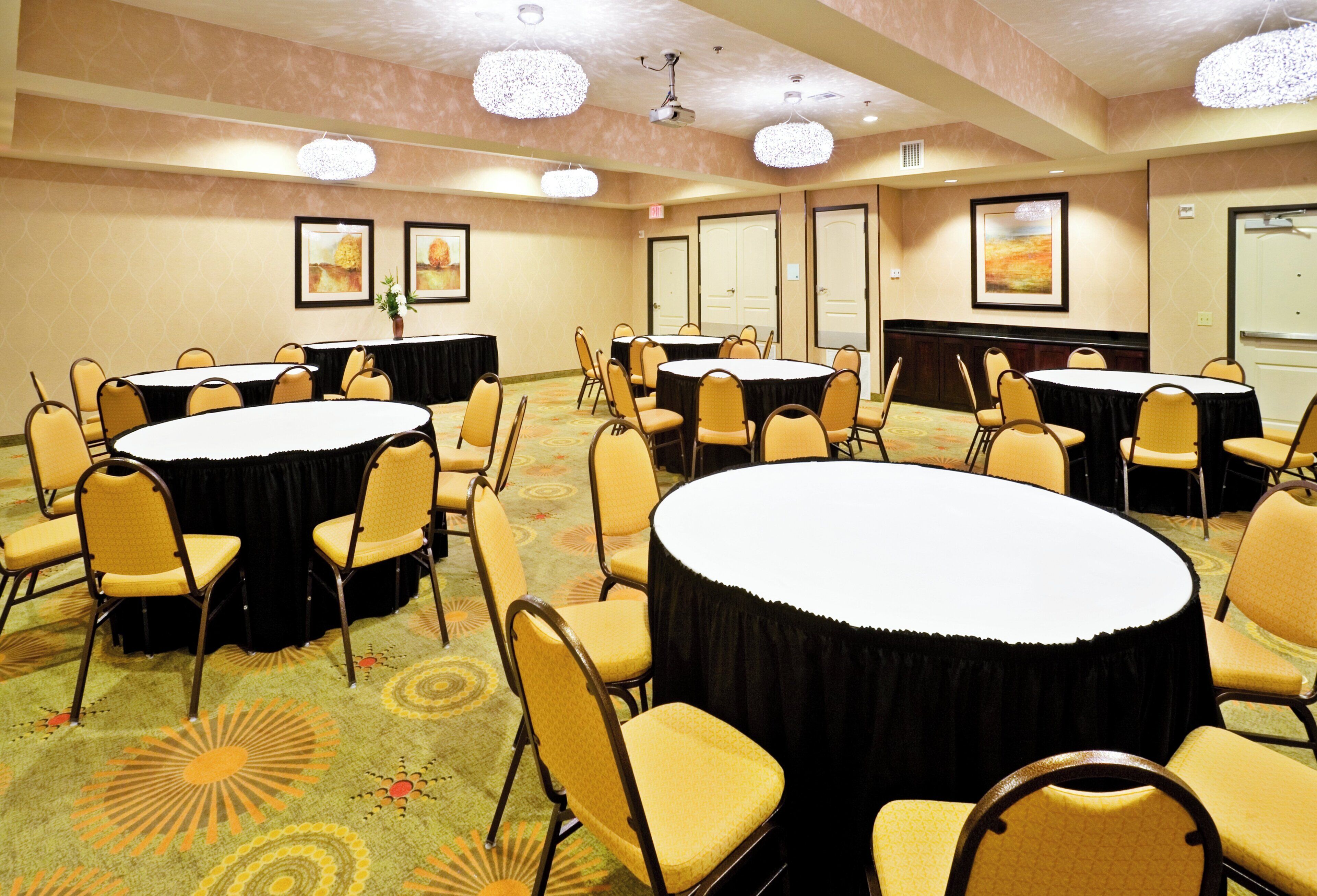 A conference room with multiple round tables and chairs, a carpeted floor, and ceiling lights.