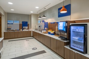 A modern breakfast area with a self-serve station, a fruit display, and a refrigerated drink dispenser. - Holiday Inn Express & Suites Dallas East - Fair Park by IHG (Dallas)