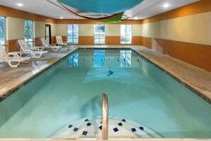 Ein Schwimmbecken mit glatter Wasseroberfläche, umgeben von Liegestühlen und einer gefliesten Wand.