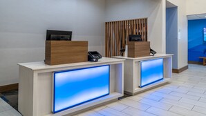 Två receptionsdiskar med inbyggda digitala skärmar, en väggpanel i trä och en modern interiördesign.