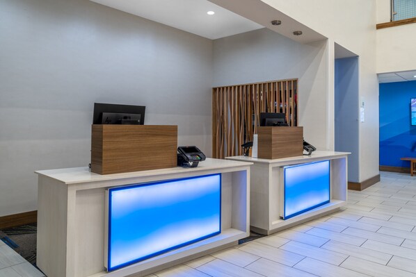 Two reception desks with built-in digital displays, a wooden panel divider, and a modern interior design. - Holiday Inn Express & Suites Dallas East - Fair Park by IHG (Dallas)