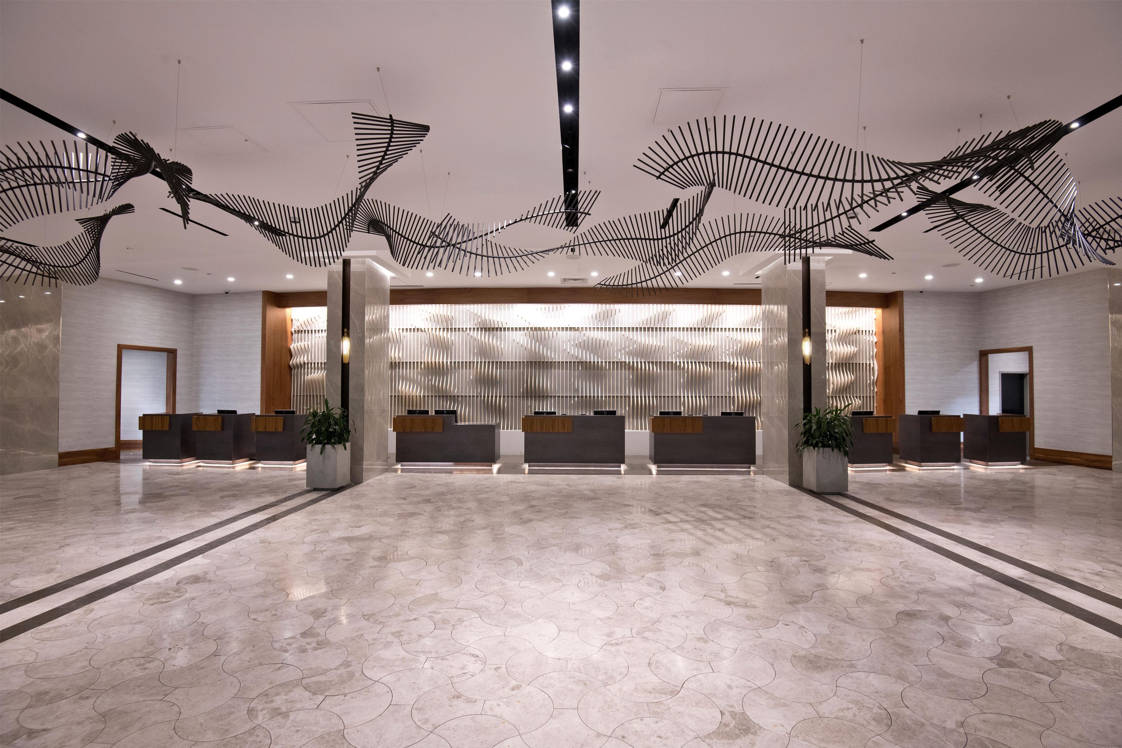 Un vestíbulo espacioso con un mostrador de recepción moderno, una planta grande y una escultura original en el techo.