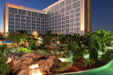 A large hotel with multiple floors, a landscaped garden with a waterfall, and a pool area.