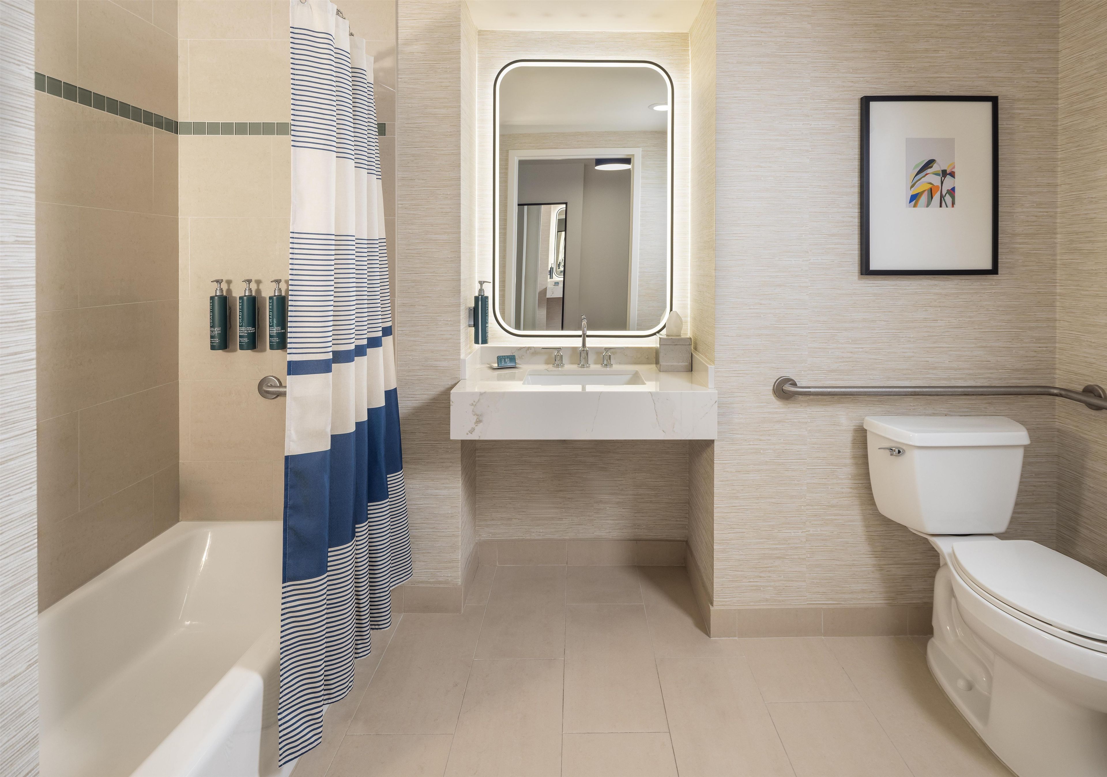Une salle de bain moderne avec une baignoire, une douche avec un rideau à rayures, un lavabo avec un miroir et des toilettes.