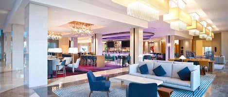A modern lobby with a bar area, seating arrangements, and a chandelier.