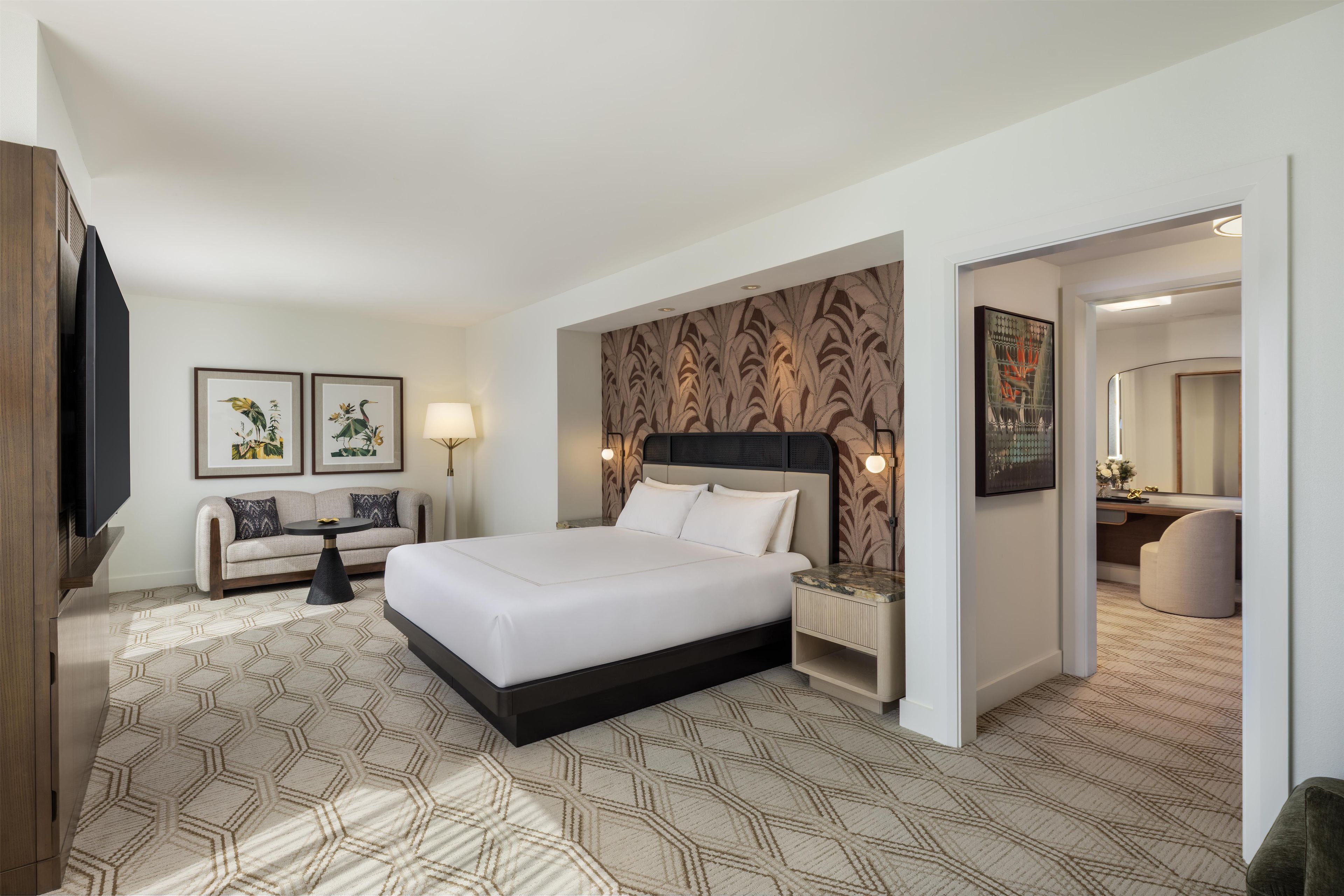 A hotel room with a large bed, a sofa, a small table, and a nightstand.