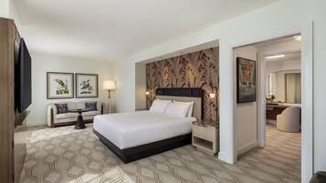 A hotel room with a large bed, a sofa, a small table, and a nightstand.