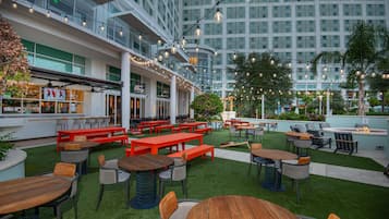 Un bar en la azotea con mesas al aire libre, vistas a un edificio moderno y un jardín bien cuidado.
