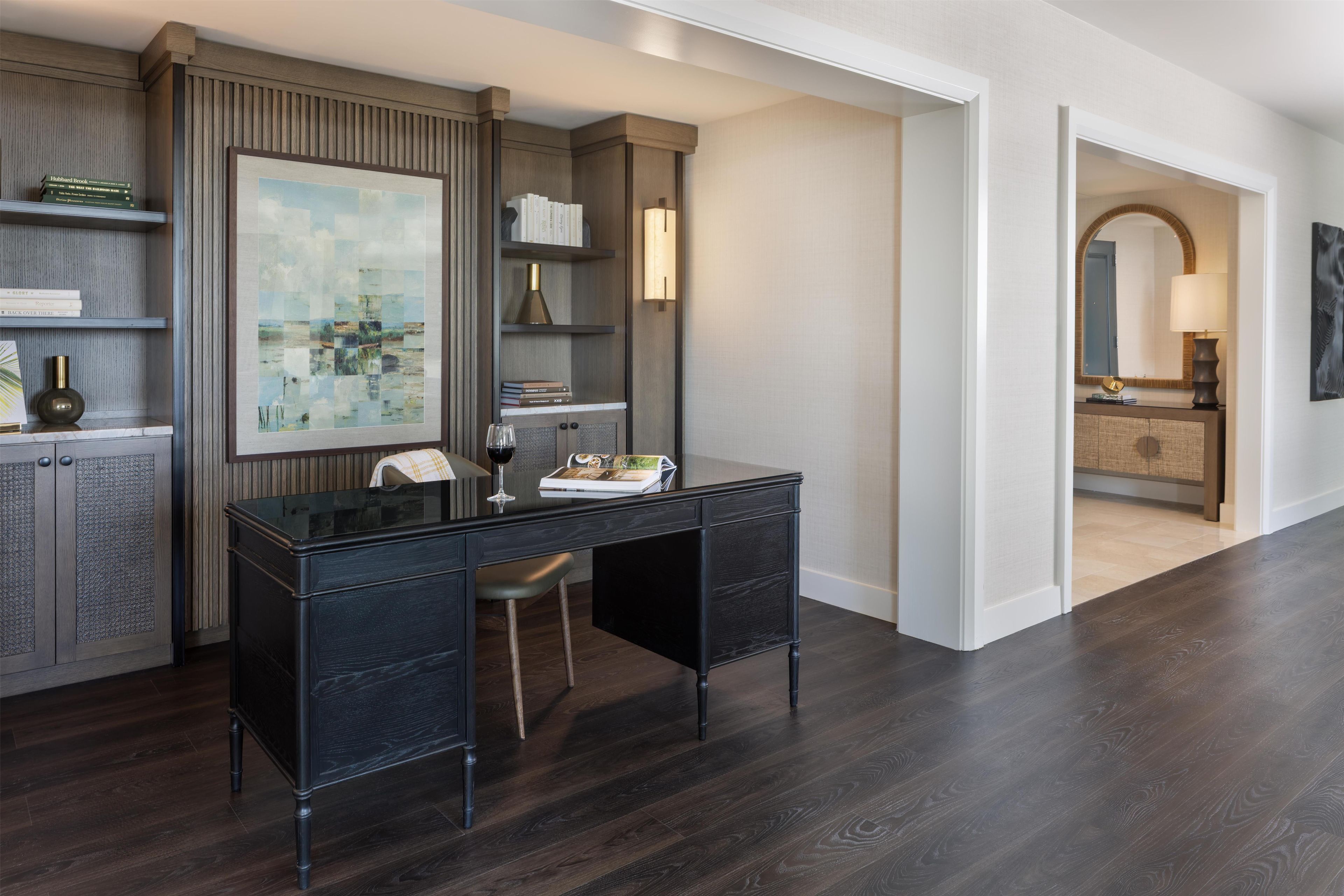 A modern room with a dark wood desk, bookshelves, a framed picture, and a mirror.