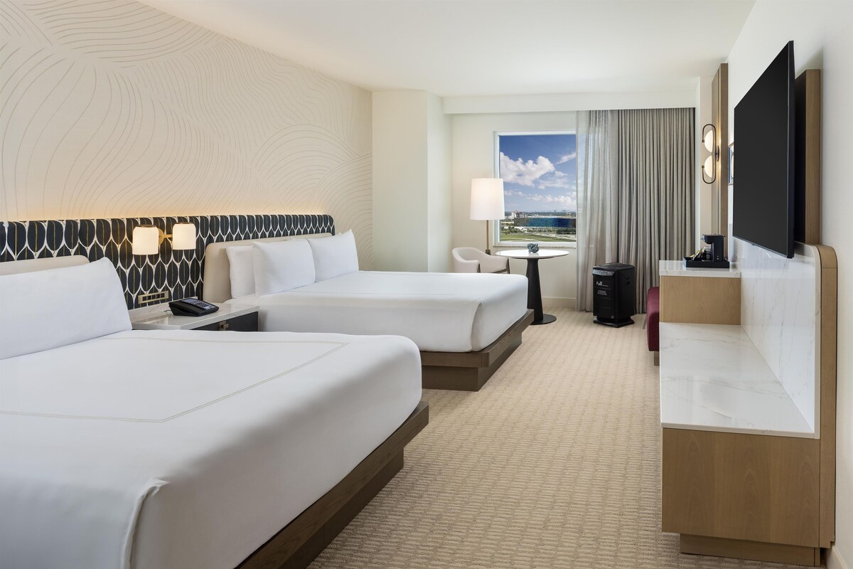 Habitación de hotel con dos camas, un escritorio, televisor, ventana con vista y lámpara.
