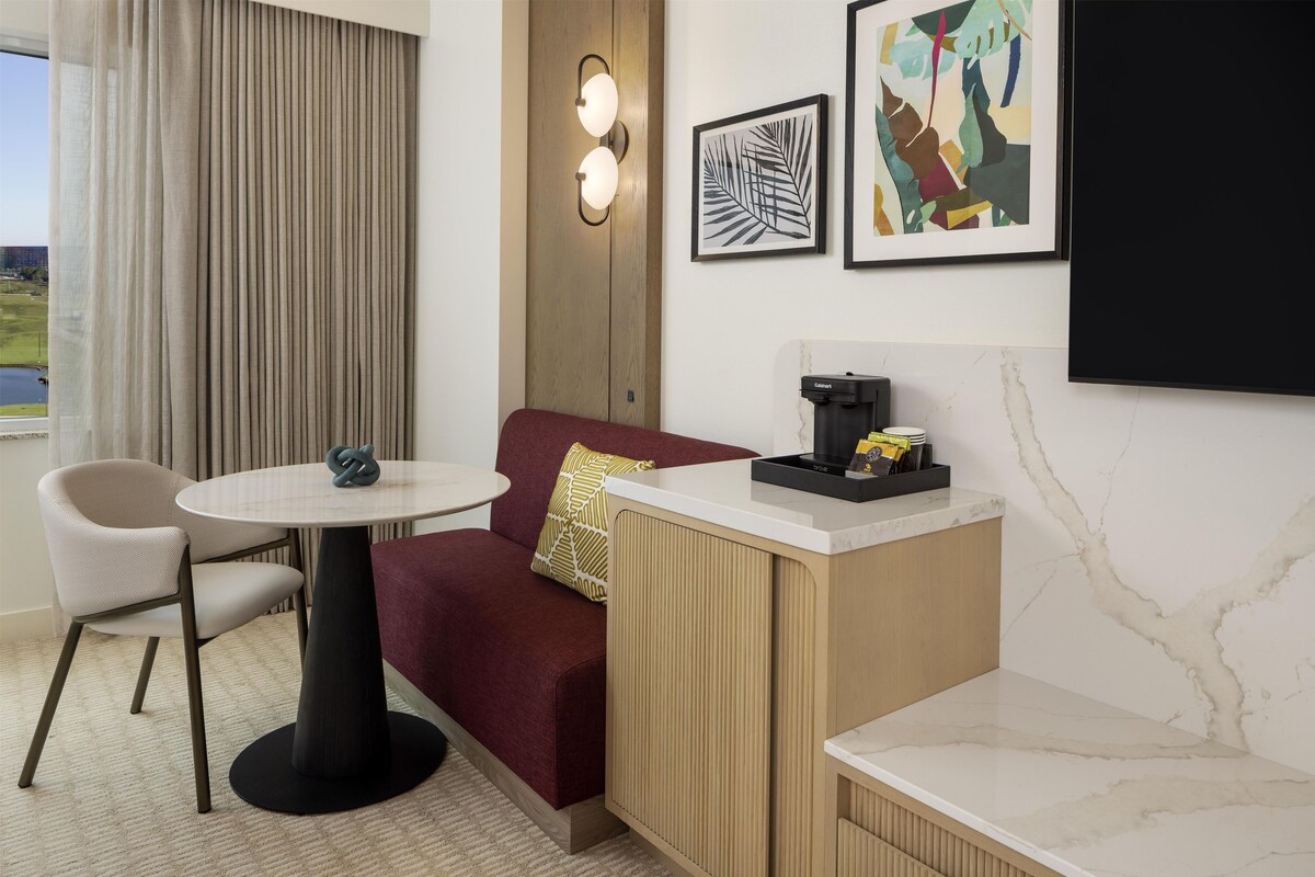 Habitación de hotel con sofá, una mesa redonda, cafetera y cuadros en la pared.