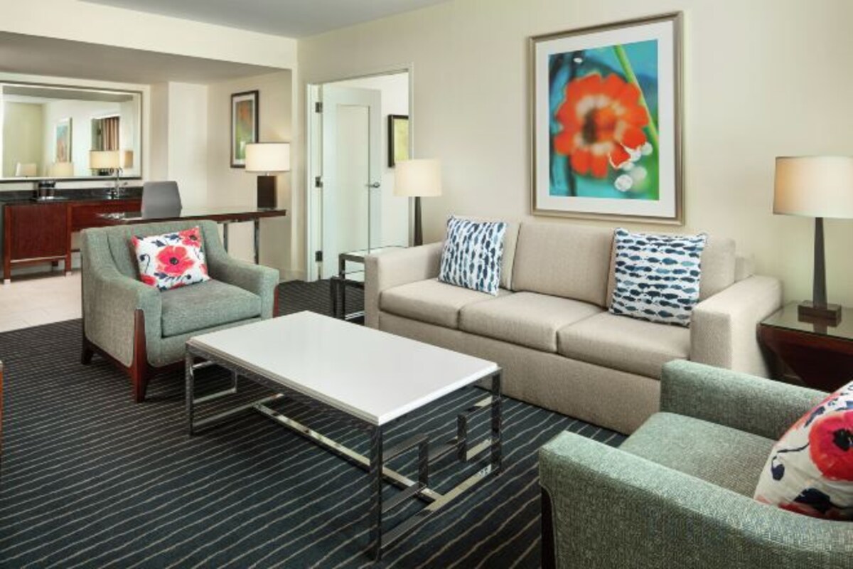Habitación de hotel con sofá, sillón y una pequeña mesa. Hay un cuadro en la pared y una lámpara en la mesita de noche.