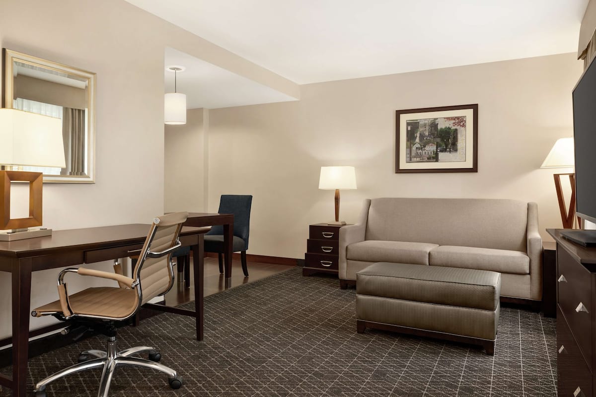 Une chambre d’hôtel équipée d’un bureau, d’une chaise, d’un canapé et d’une petite table de chevet avec une lampe.
