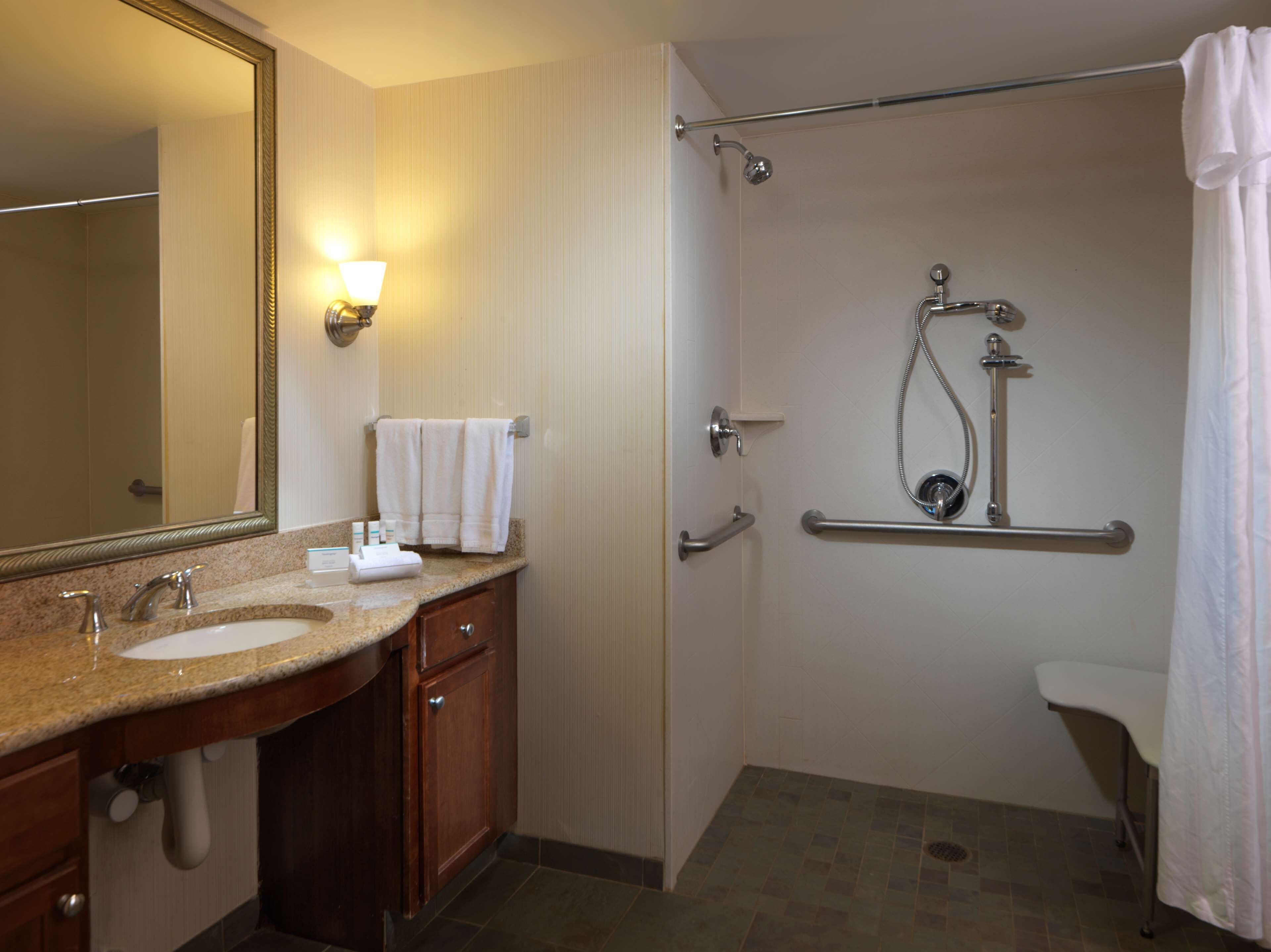 A bathroom with a sink, mirror, towel rack, shower, and grab bars.