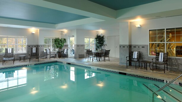 Une piscine entourée de grandes baies vitrées, avec des chaises longues et un espace repas.