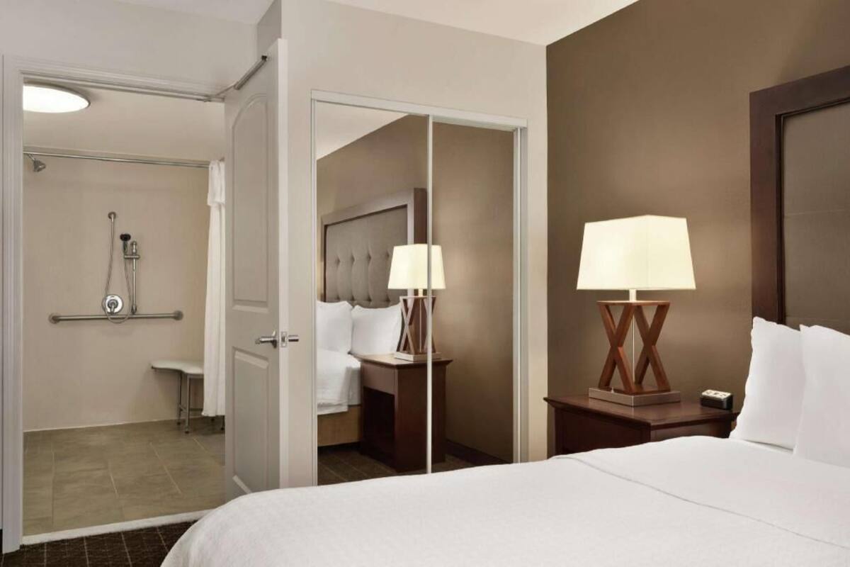 Une chambre d’hôtel avec un lit, une table de chevet, une lampe et un miroir.